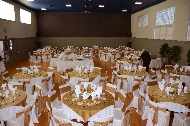 The auditorium, featuring elegantly arranged round tables with white tablecloths and gold coloured accents, ready for a formal gathering.