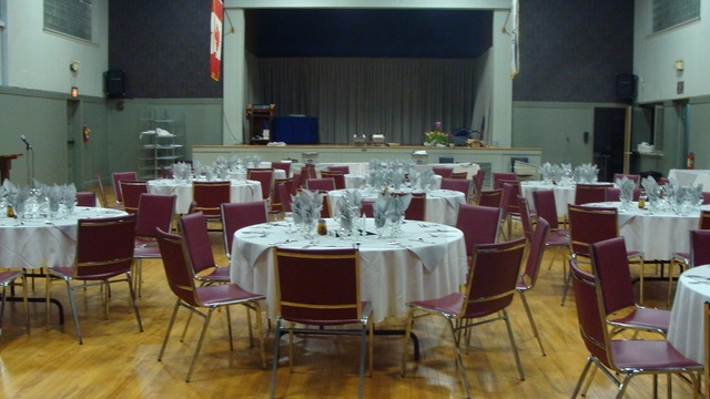 A view of the auditorium set up for an event, featuring several round tables covered with white tablecloths and arranged with chairs.